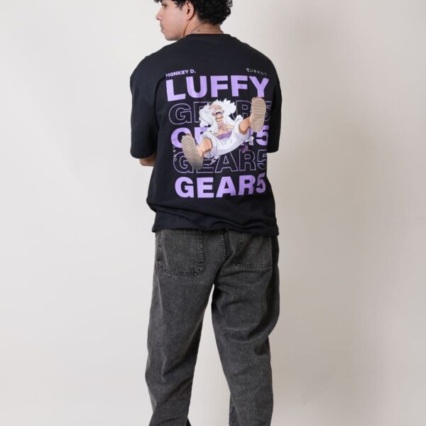 Back view of a black oversized One Piece T-shirt featuring Monkey D. Luffy Gear 5 anime graphic with bold purple 'LUFFY GEAR 5' text. Worn by a male model with curly hair, paired with black acid-washed jeans and white sneakers. Ideal for anime fans and streetwear lovers.